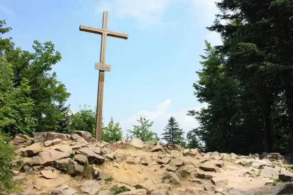 Drewniany krzyż na skalistym szczycie, najwyższy szczyt w górach świętokrzyskich, otoczony zielenią drzew.